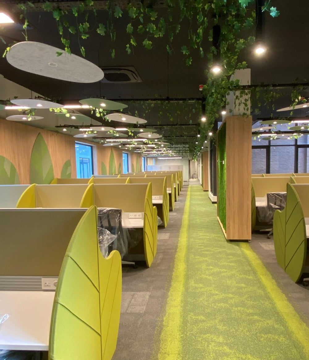 Open-plan workspace with green desk partitions and suspended acoustic ceiling panels